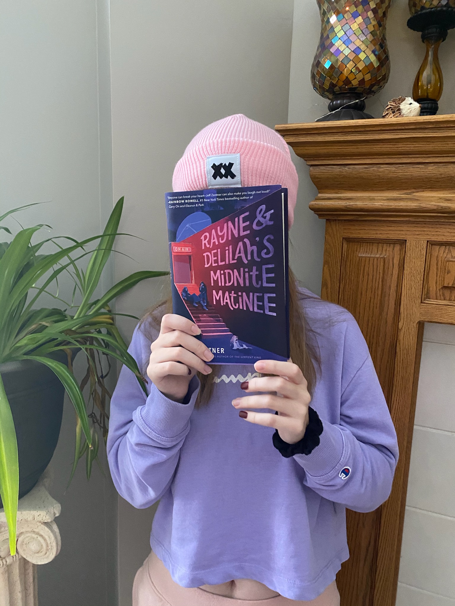 Sydney holding the book Rayne and Delilah's Midnite Matinee by Jeff Zentner in front of her face